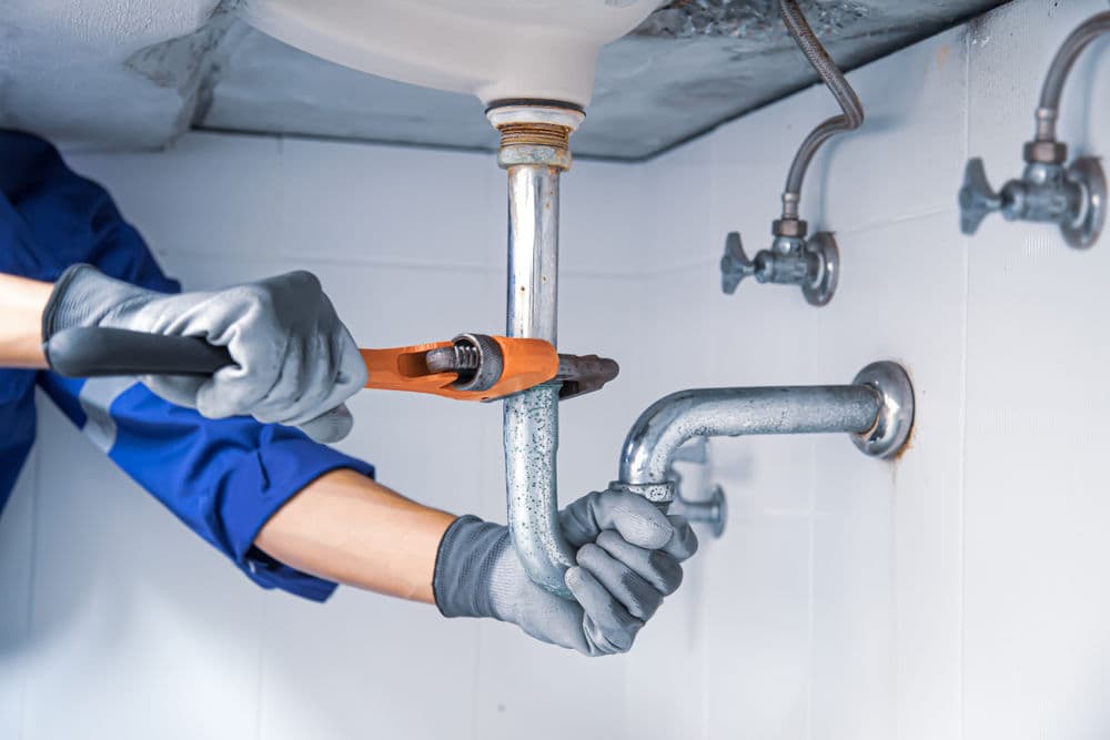 Plumber using a wrench to repair pipes under a sink in a residential setting.